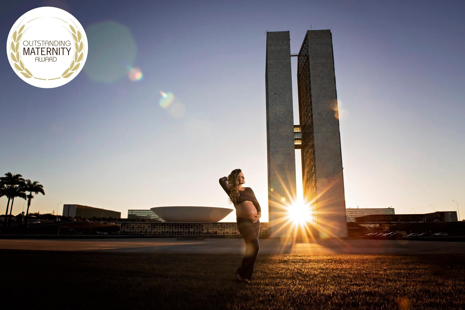 Mãe grávida posando em frente ao Congresso Nacional de Brasília ao pôr do sol, com destaque para a maternidade e o prêmio Maternity Award, simbolizando a importância da gestação.
